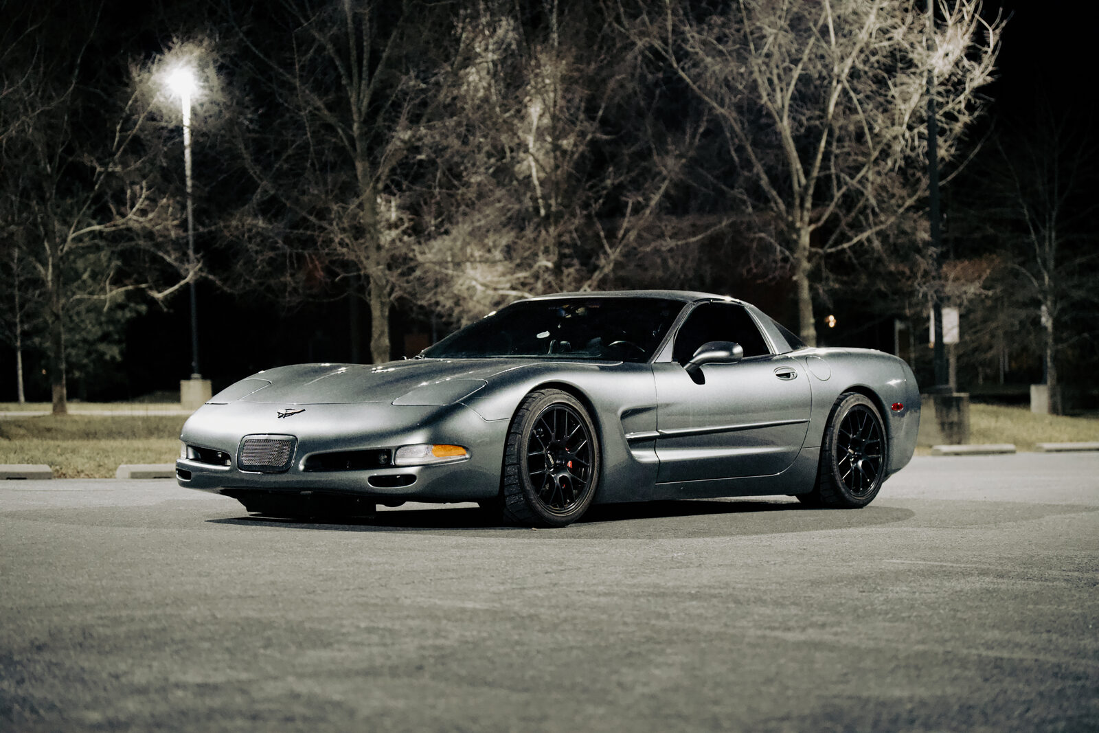 A grey Corvette C5 parked under a streetlight at night.