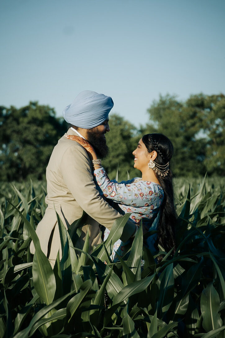 A couple in a close embrace facing each other in a cornfield.