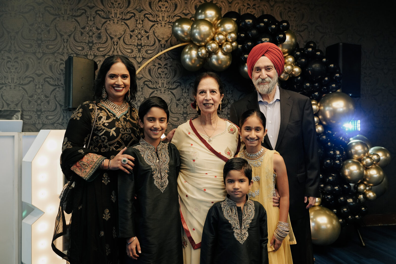 A family group portrait at a celebration with gold and black balloon decor.