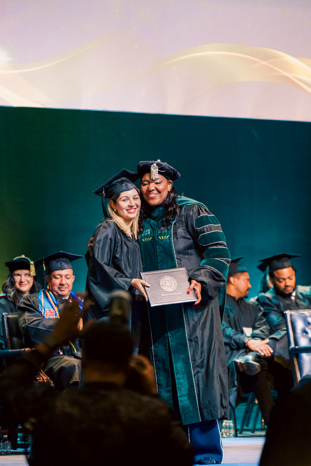 A graduate embracing a university official on stage while receiving her diploma.