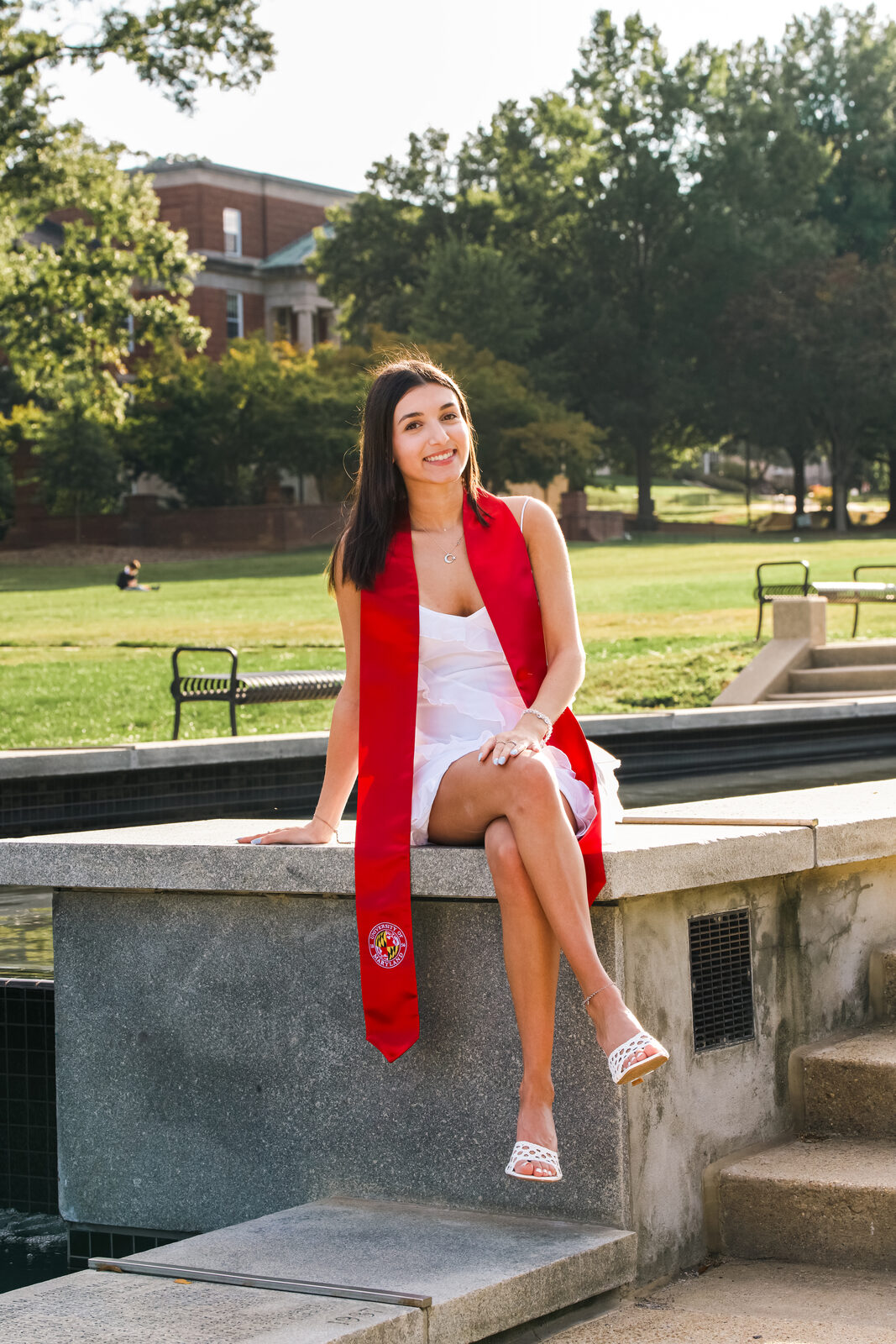 A graduate seated on a low wall by a campus fountain at the University of Maryland.