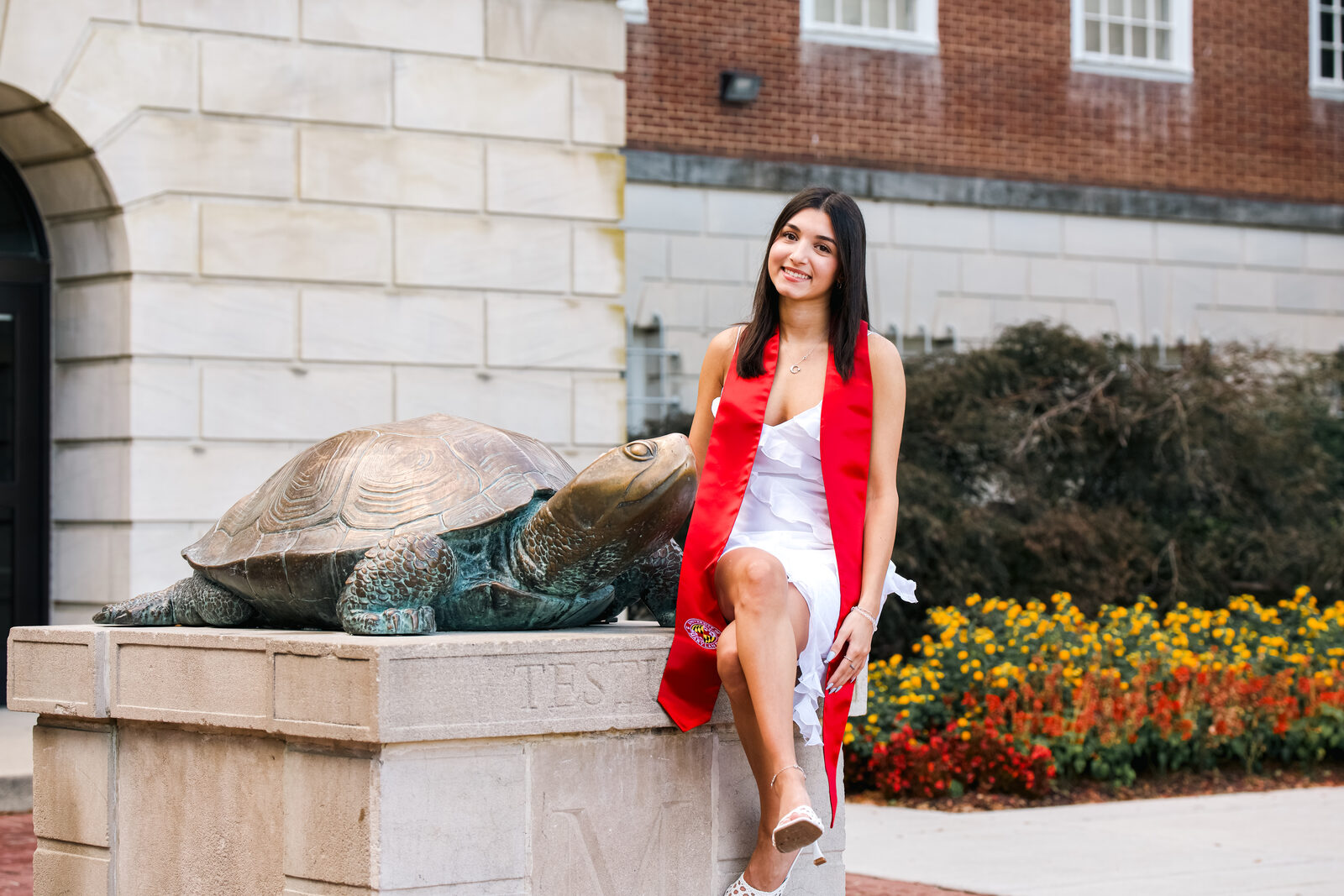 A graduate posing beside the Testudo turtle statue, smiling.