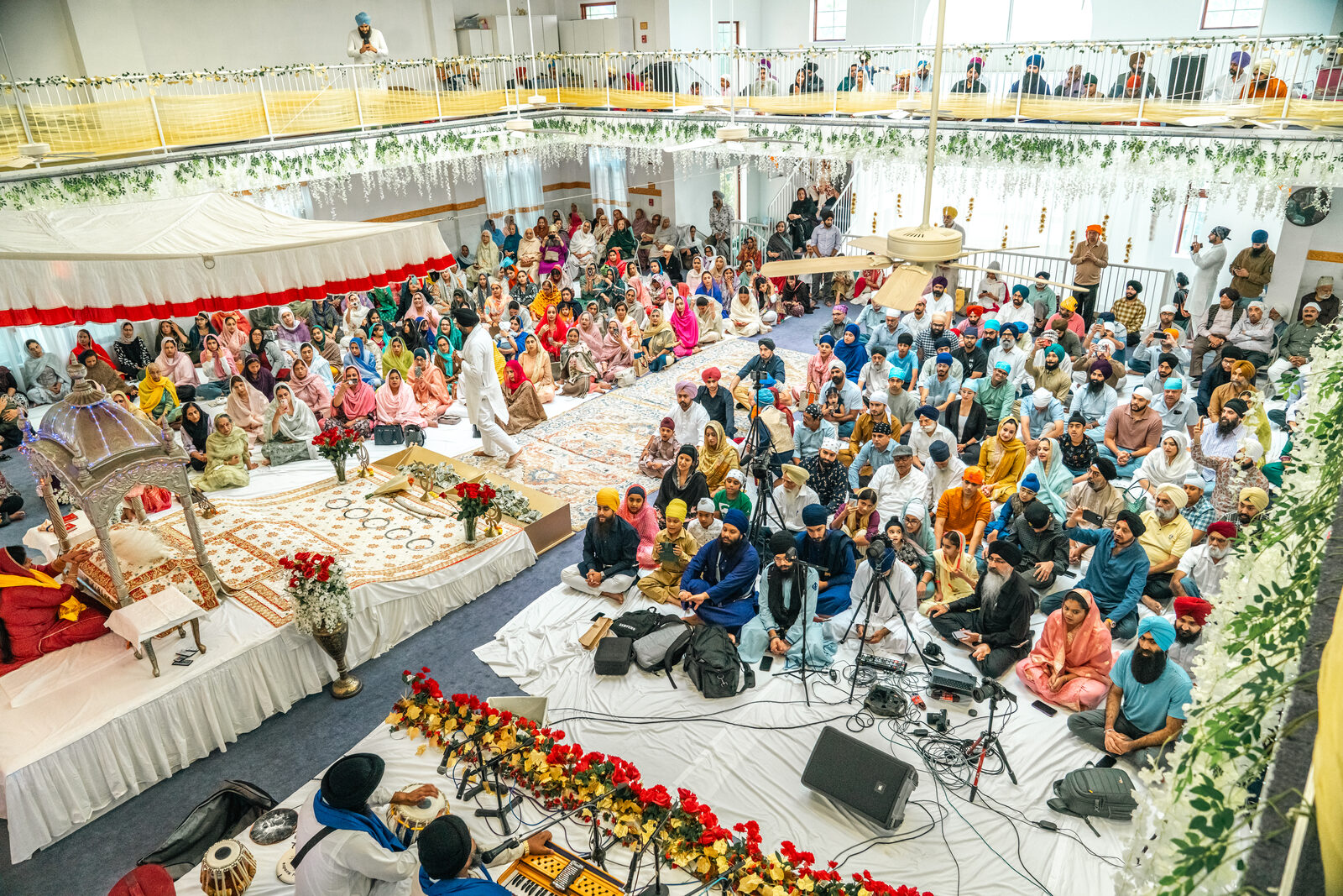 A wide aerial view of the gurdwara hall filled with the community during the celebration.