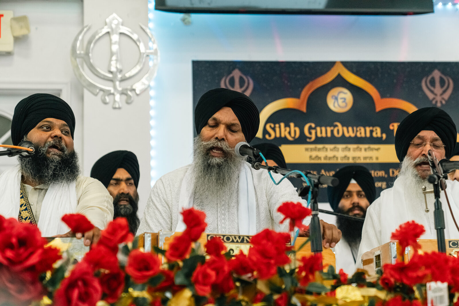 Kirtan performers on stage beneath the gurdwara sign.