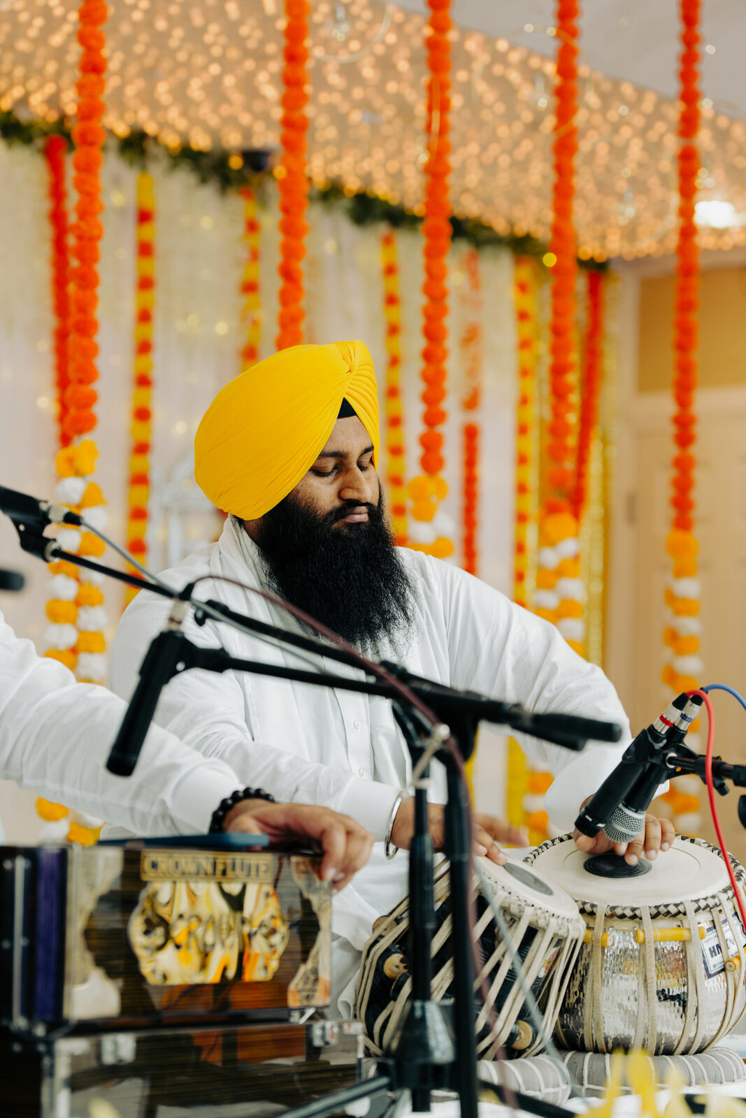 A tabla player performing in front of a marigold garland backdrop.