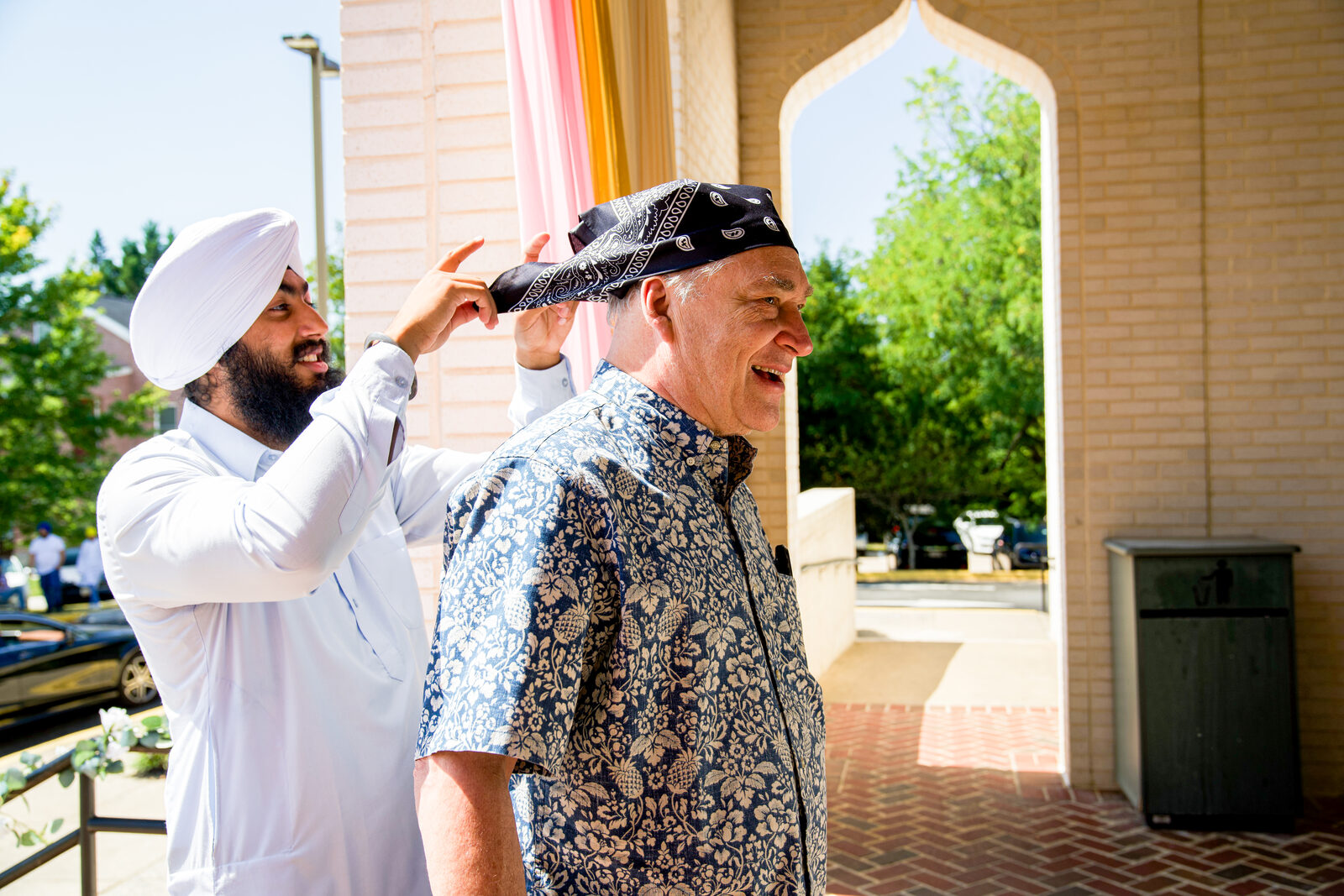 A candid moment of one man tying a bandana on another outside the gurdwara.