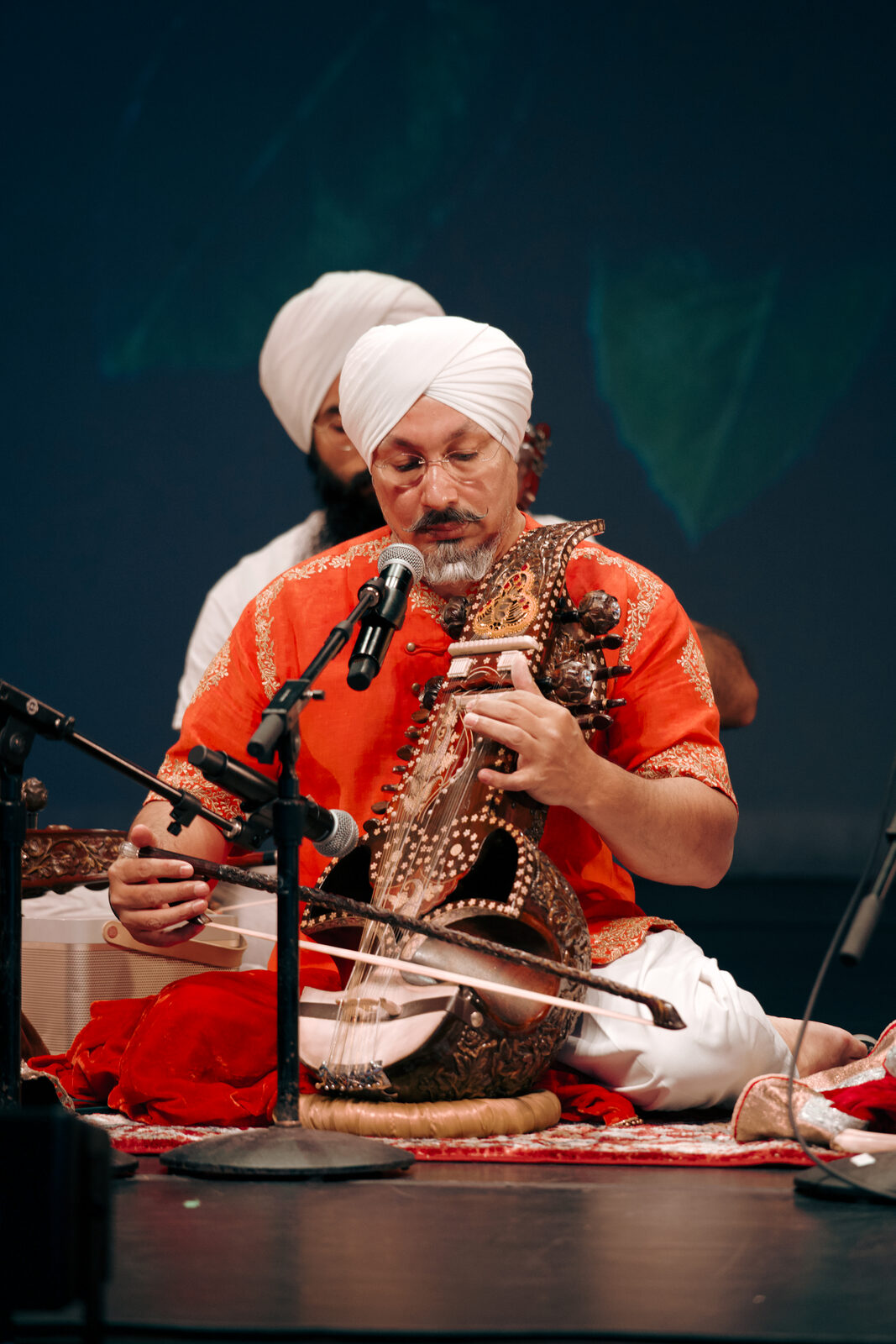 A musician in orange playing a sarangi, close-up.