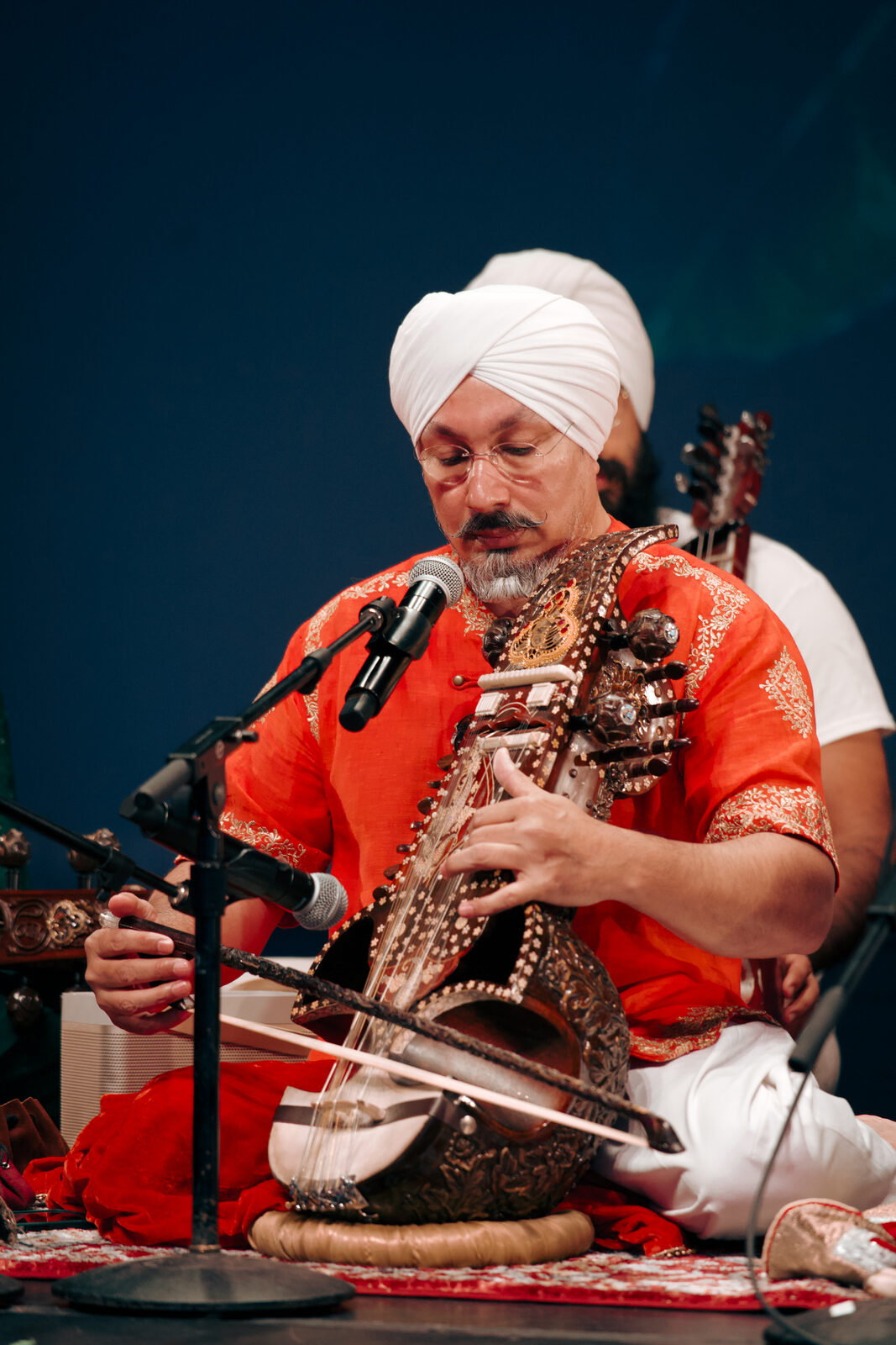 A close portrait of the sarangi player mid-performance.