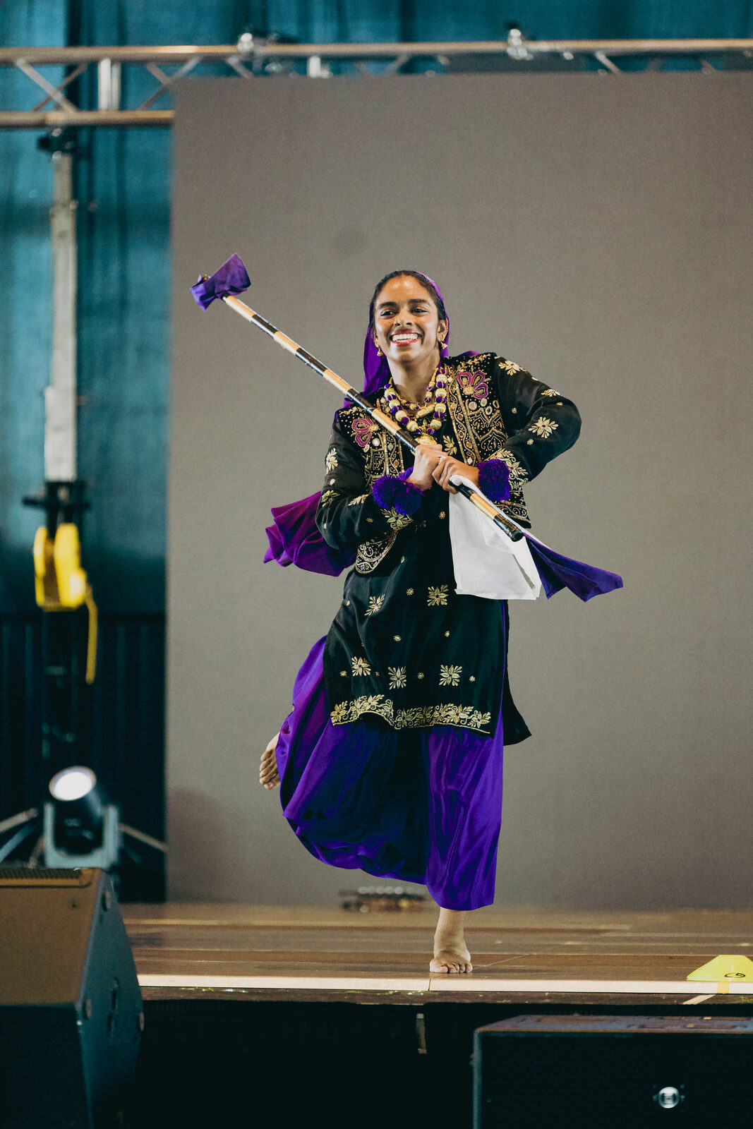 A Giddha performer captured mid-jump with a stick prop.