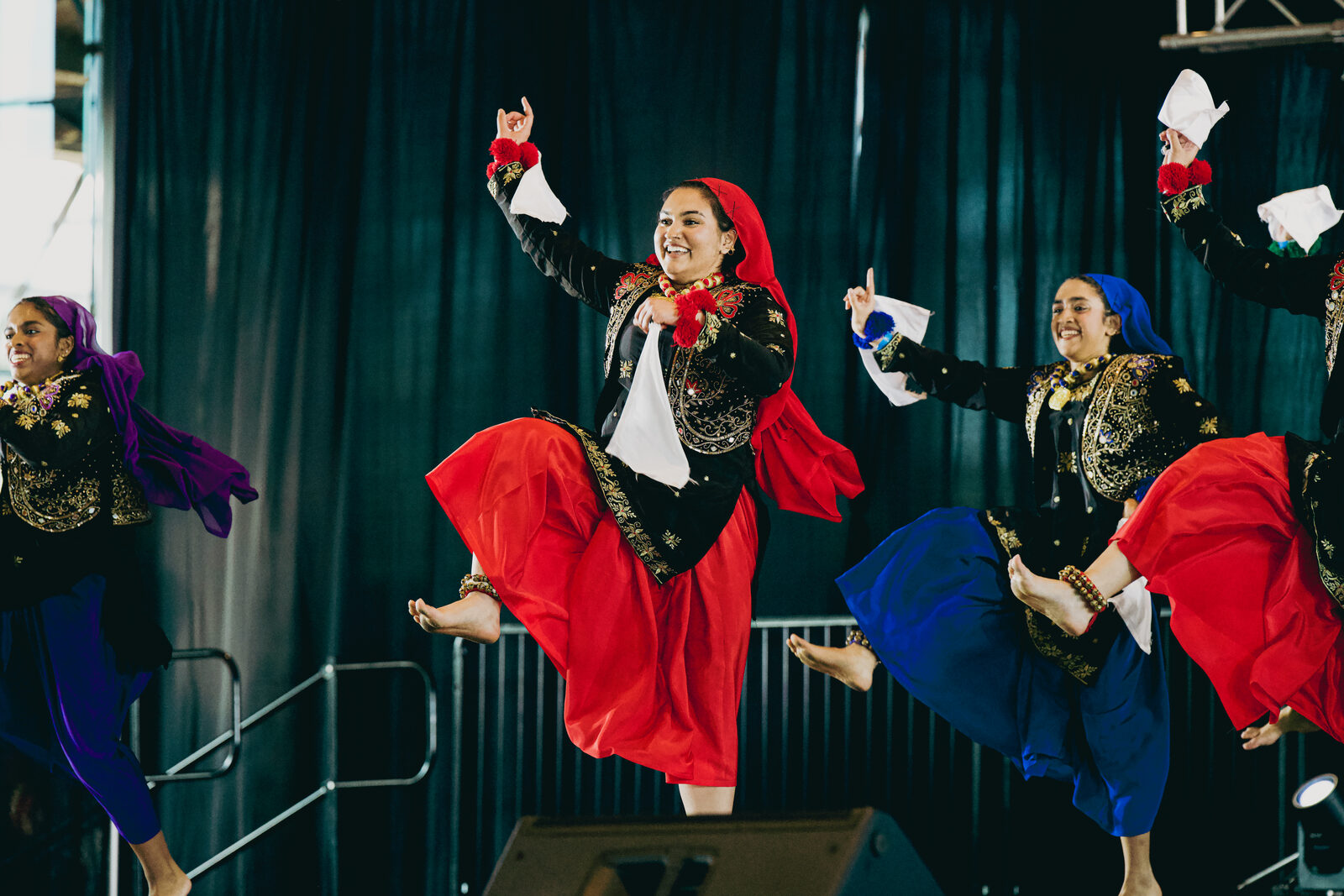 Two Giddha performers mid-jump in red and blue costumes.