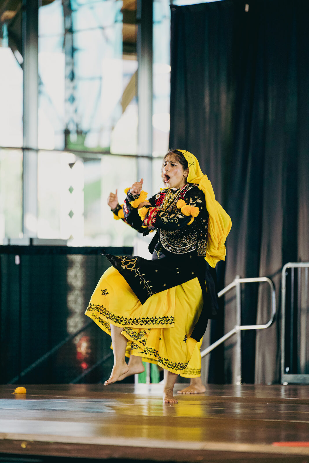 A Giddha performer in a yellow and black ensemble mid-routine.