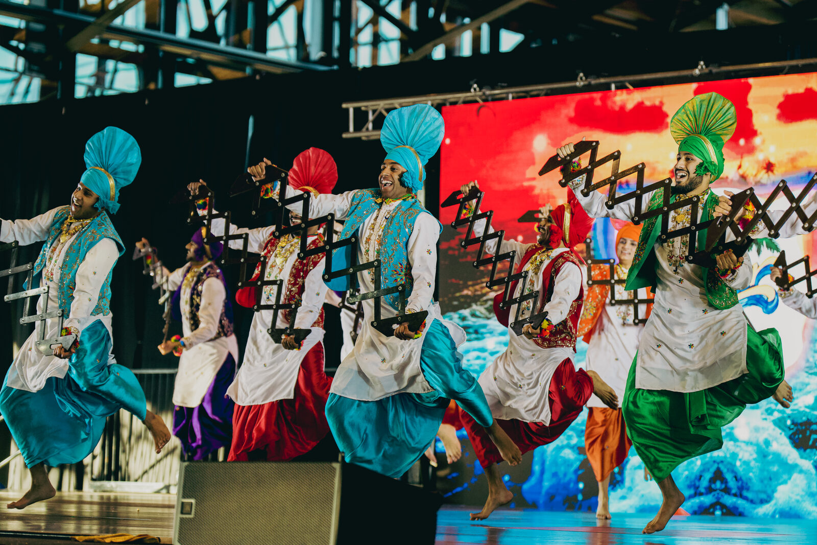 A Bhangra team performing together in blue, red, and turquoise costumes.