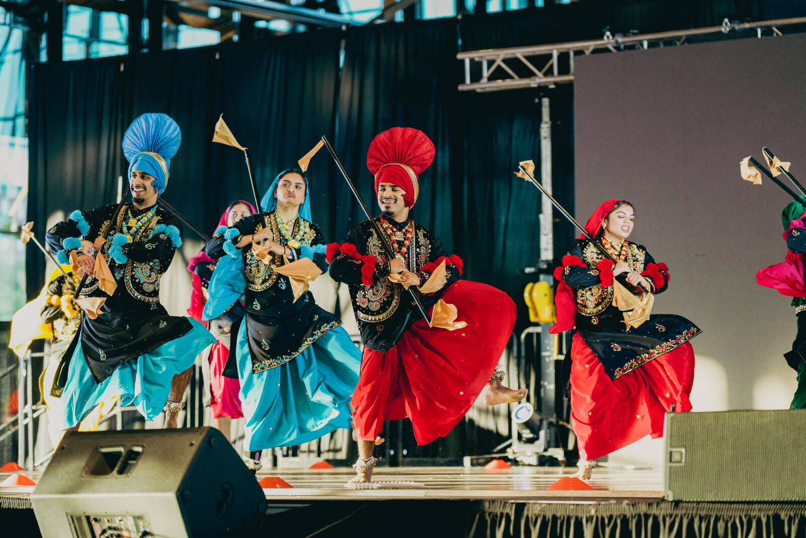 Bhangra dance team mid-jump in a colorful formation on stage.