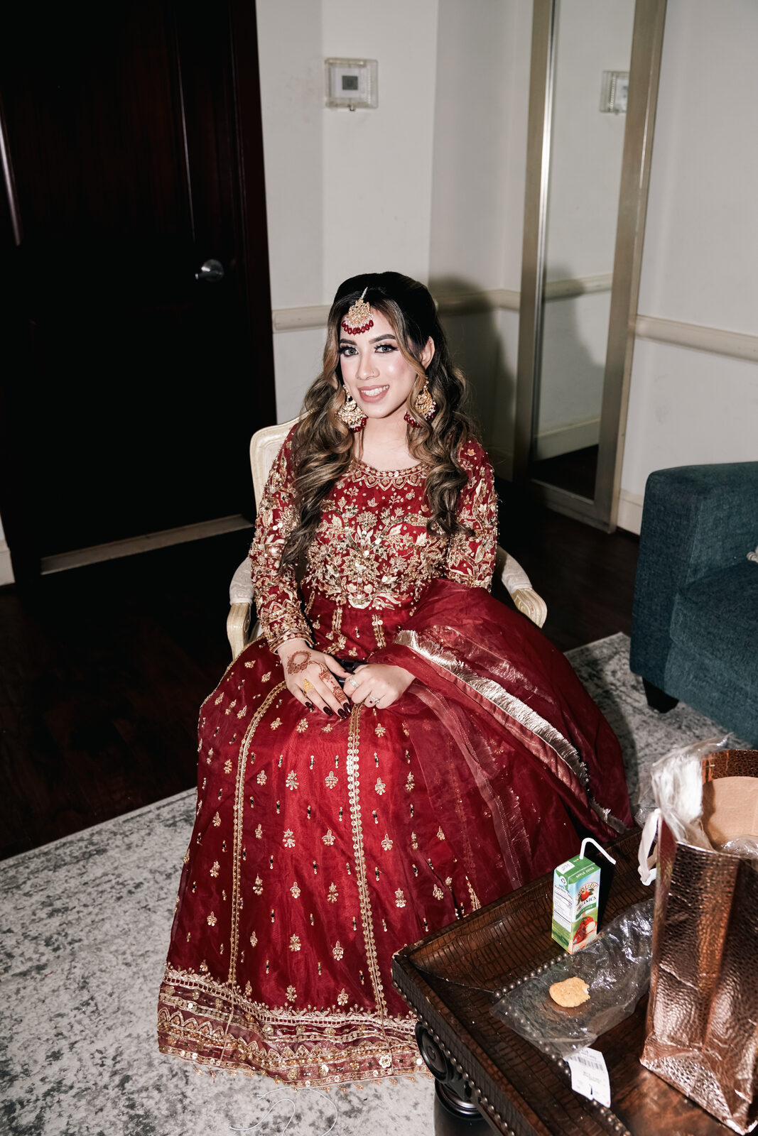 Bridal portrait, seated in a red and gold lehenga.