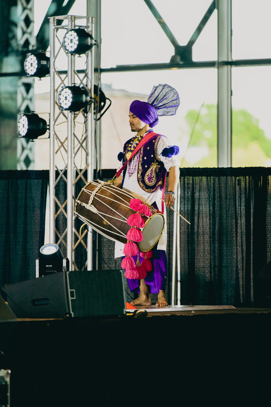 A dhol player performing on stage in traditional dress.