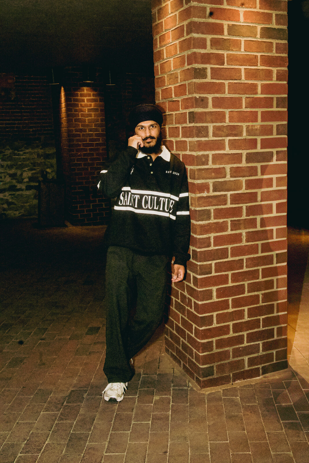 A portrait shot leaning against a brick pillar at night.