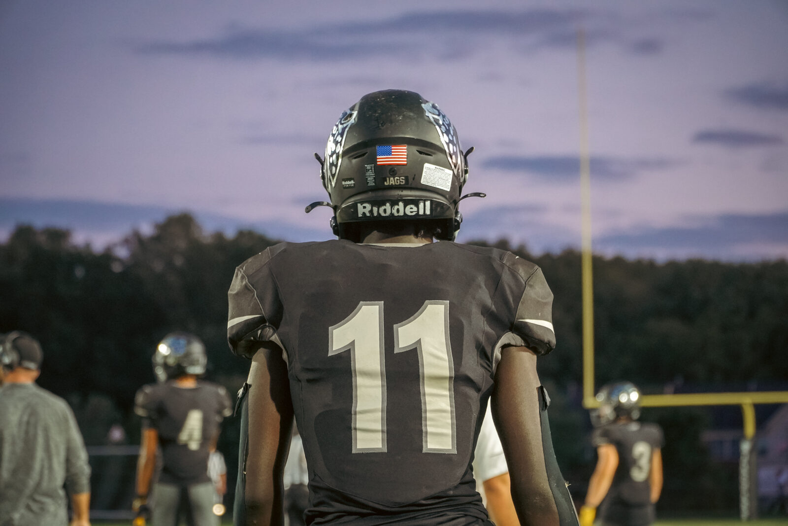 A football player viewed from behind on the field at dusk.