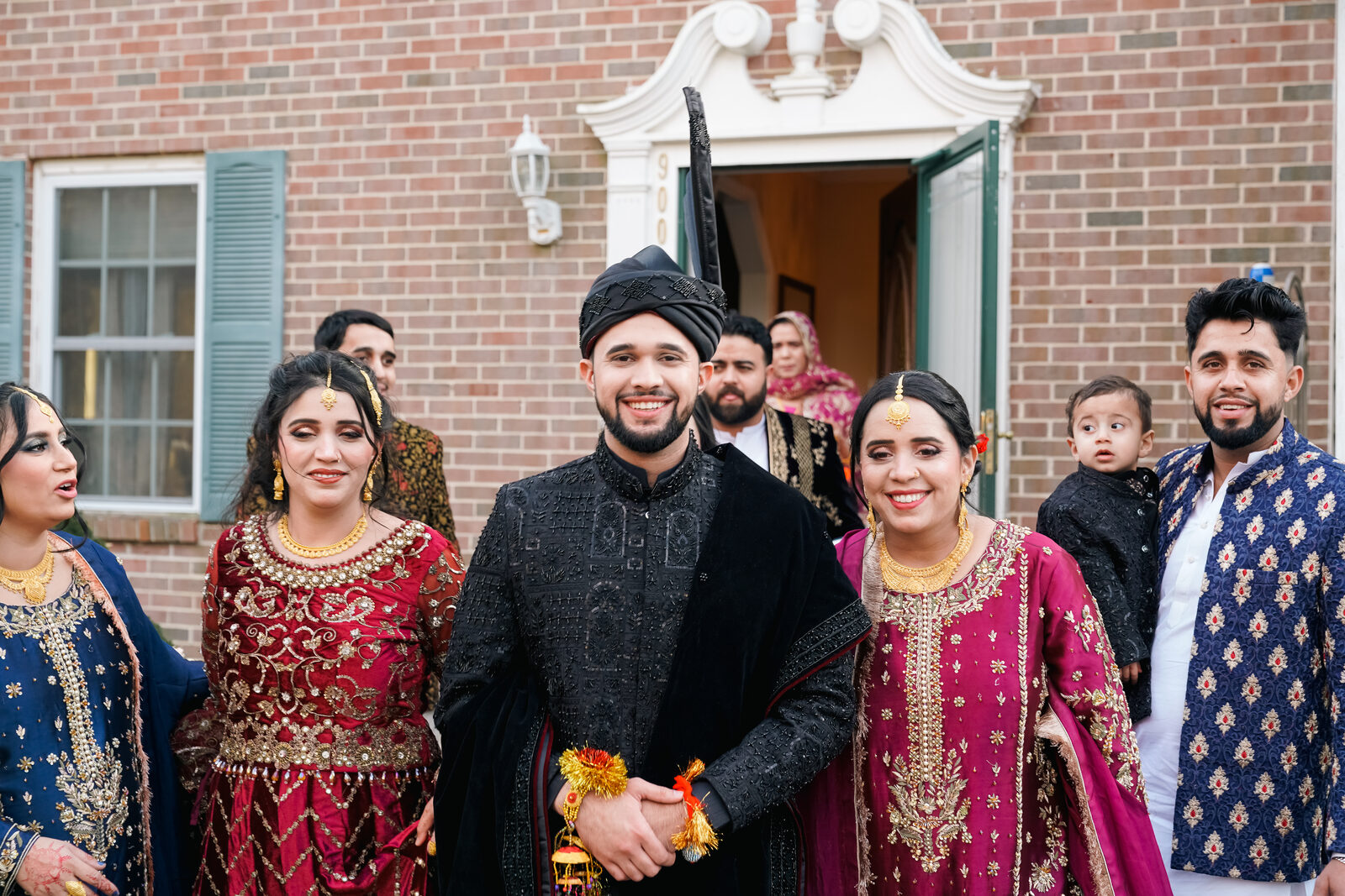A family group portrait outside a brick house on the wedding day.